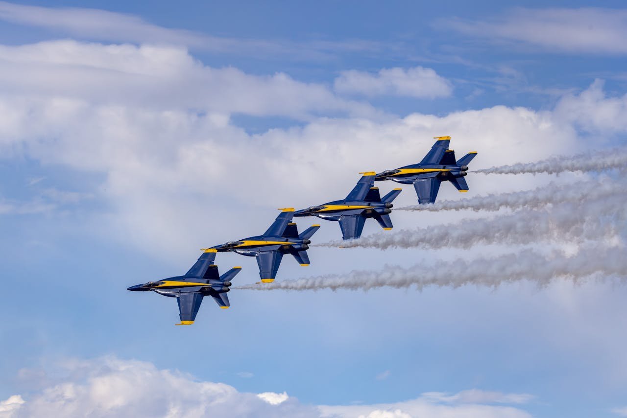 Four Blue Angels jets in precise aerobatic formation against a bright sky.