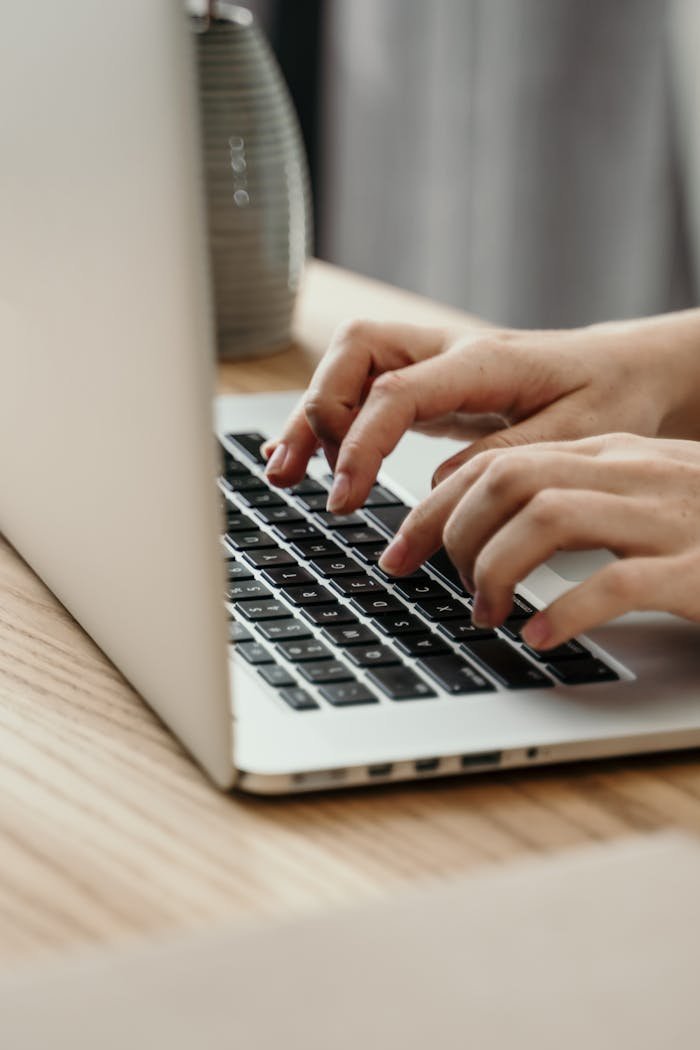 Hands typing on a laptop keyboard in an indoor setting, emphasizing productivity and technology.