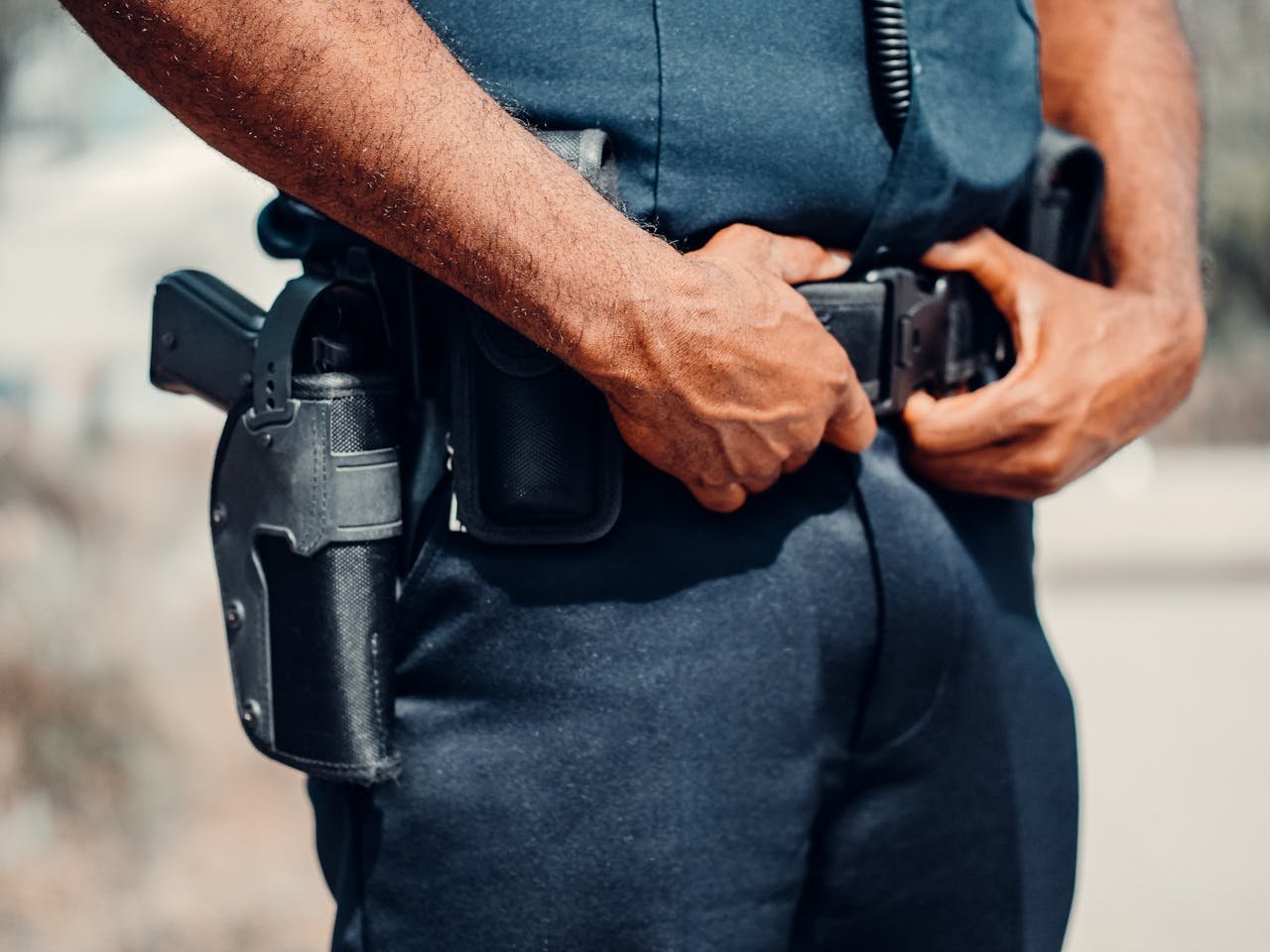 A police officer adjusts their utility belt outdoors, showcasing law enforcement gear and uniform.