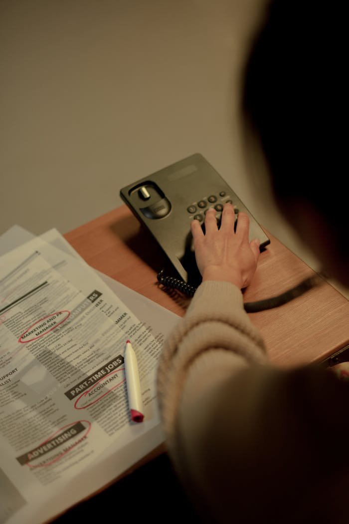 services-03 Woman using a phone to inquire about job postings, newspaper and pen on a table.